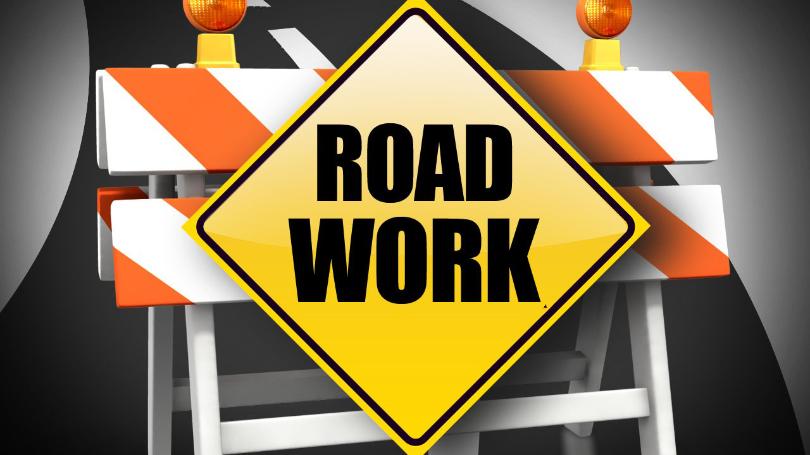 Orange/white construction barrier with yellow road work sign written with black letters