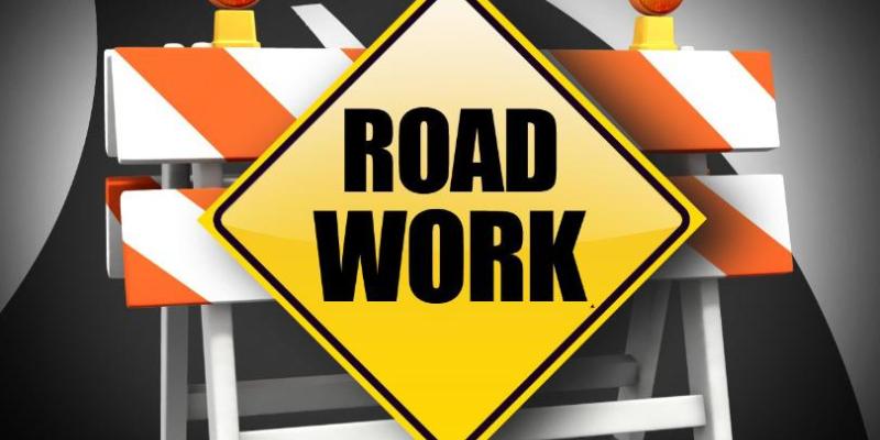 Orange/white construction barrier with yellow road work sign written with black letters